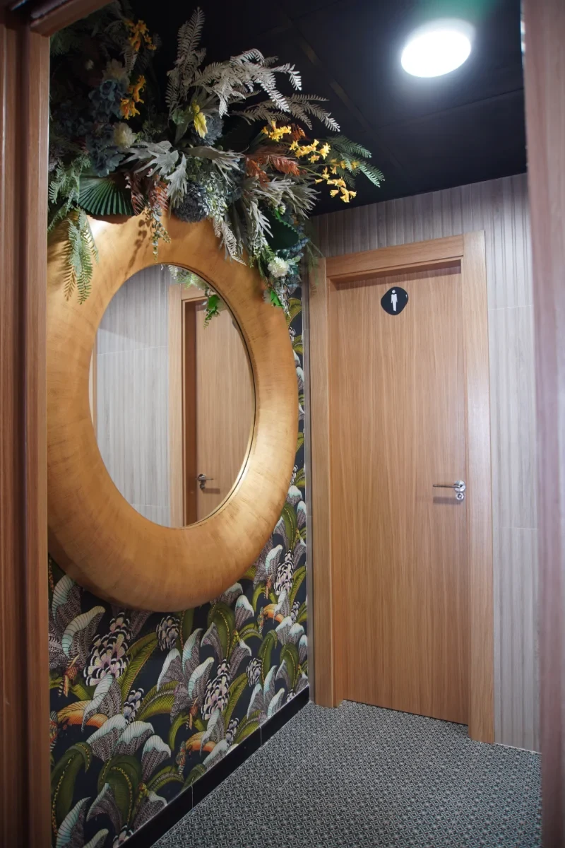 Aseo del restaurante Los Dos en El Campello, con puertas de madera y papel pintado vegetal