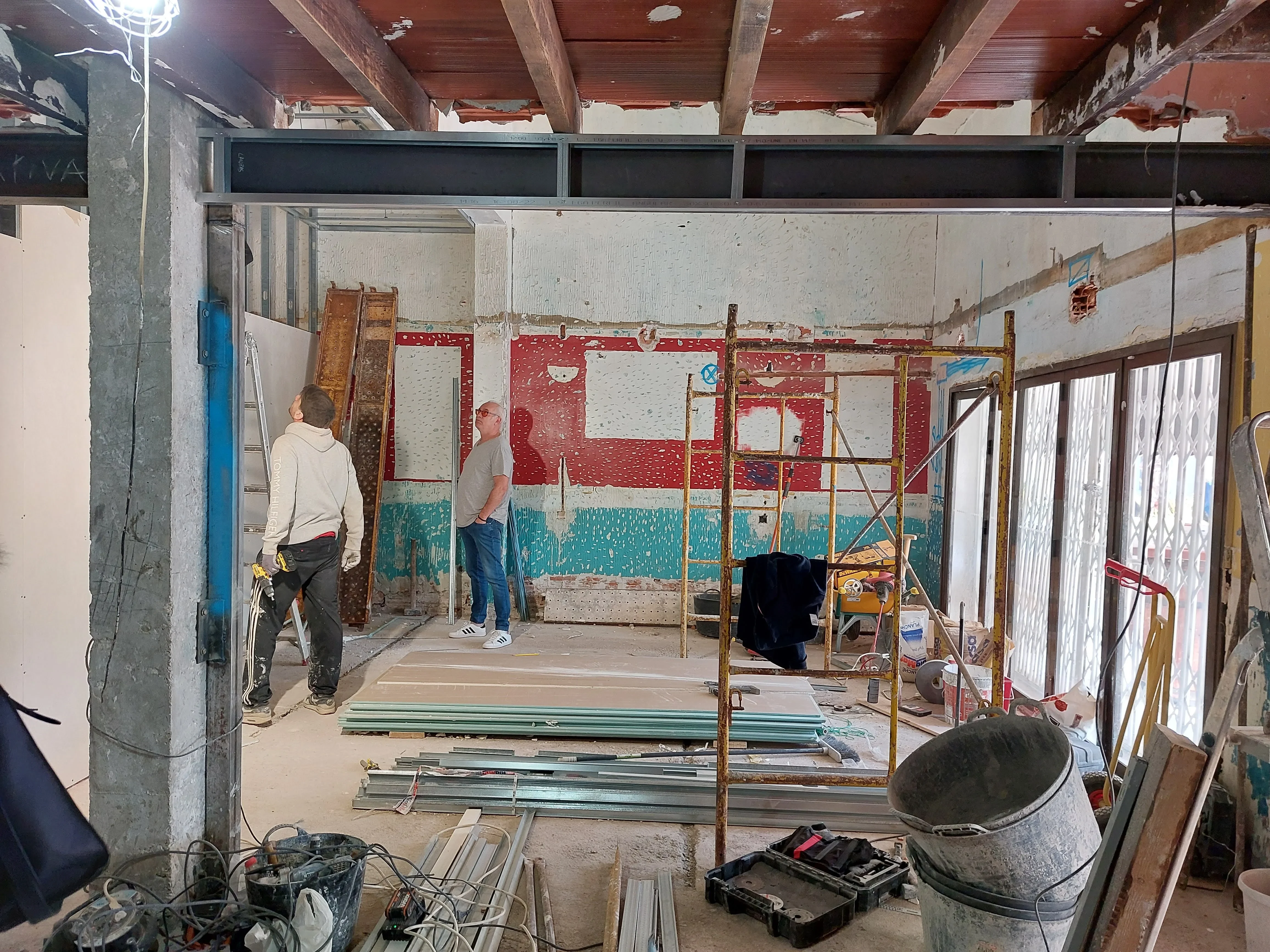 Interior del restaurante Los Dos en El Campello con la demolición ya empezada: la nueva viga de acero que recoge las antiguas vigas de madera del techo cruza el espacio, tras retirar el tabique que partía la sala, con el antiguo alicatado parcialmente a la vista