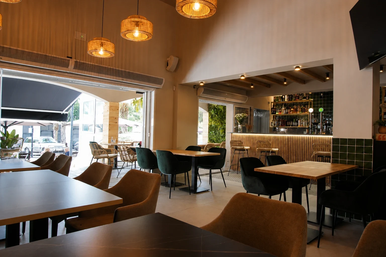 Interior finalizado del restaurante Los Dos en El Campello con mesas de madera, lámparas cálidas, barra con azulejo verde y terraza abierta al fondo