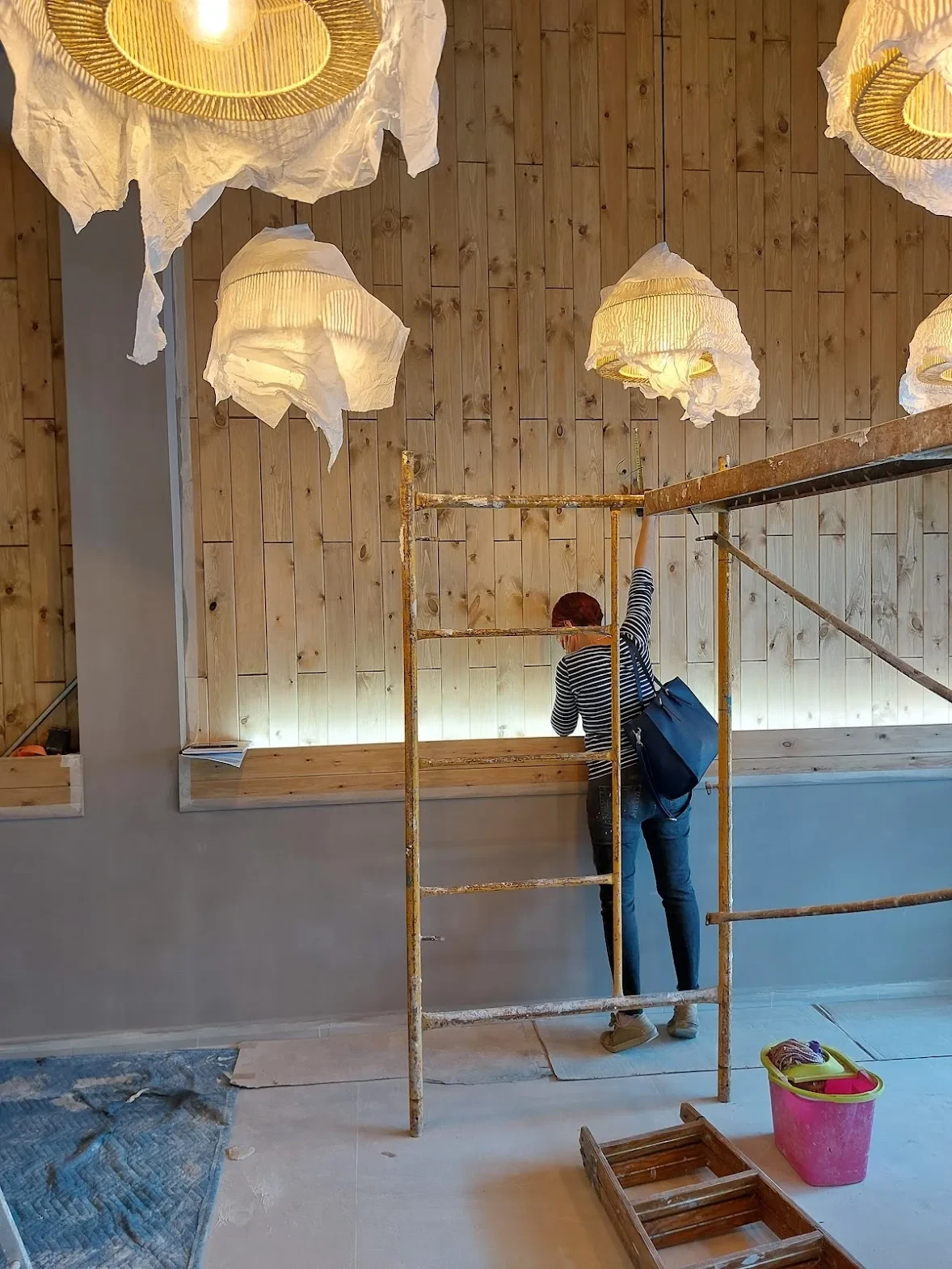 Operaria trabajando desde un andamio en la pared de madera del restaurante Los Dos en El Campello, bajo las lámparas de papel