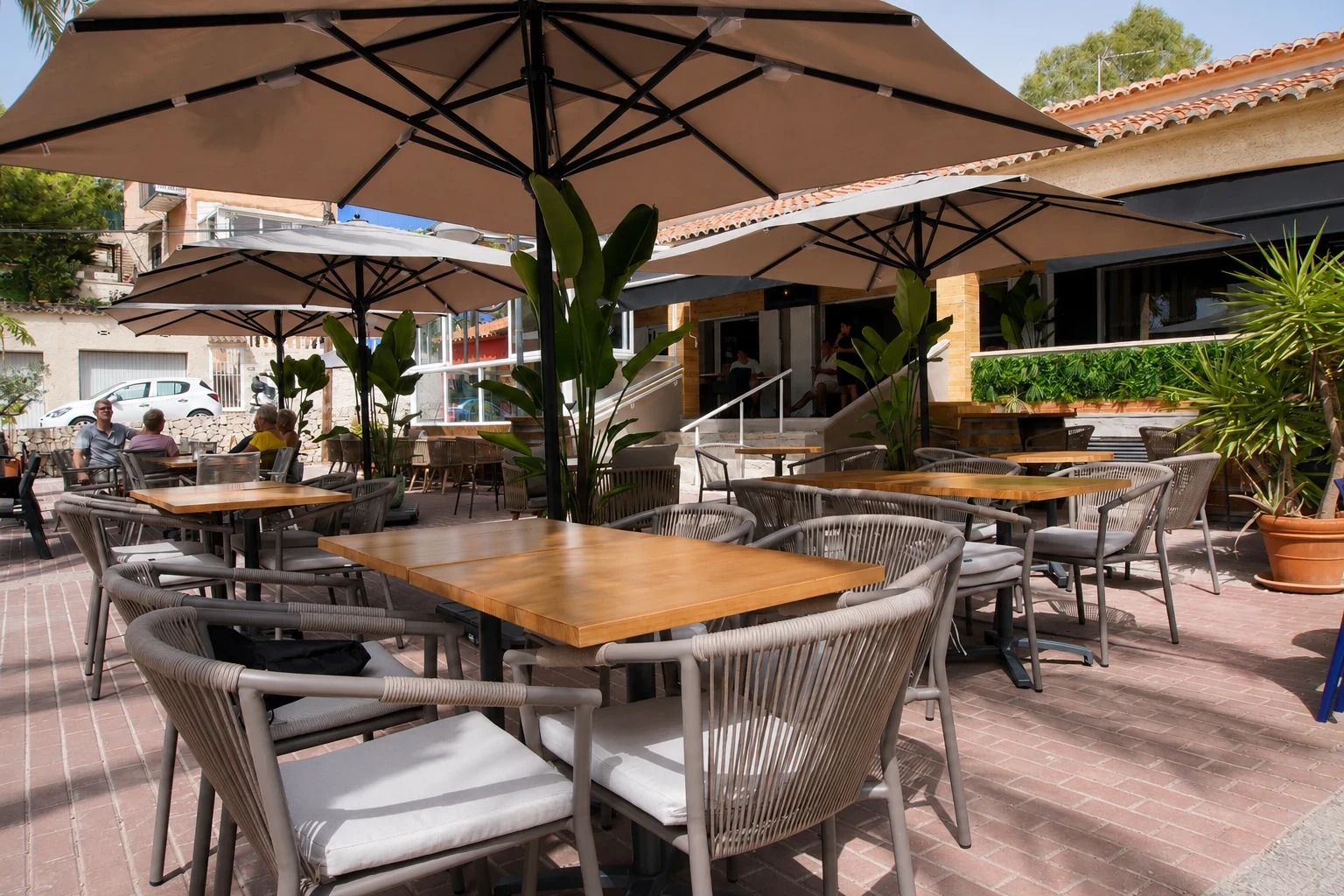 Terraza finalizada del restaurante Los Dos en El Campello con mesas de madera, sillas de exterior, sombrillas grandes y vegetación mediterránea