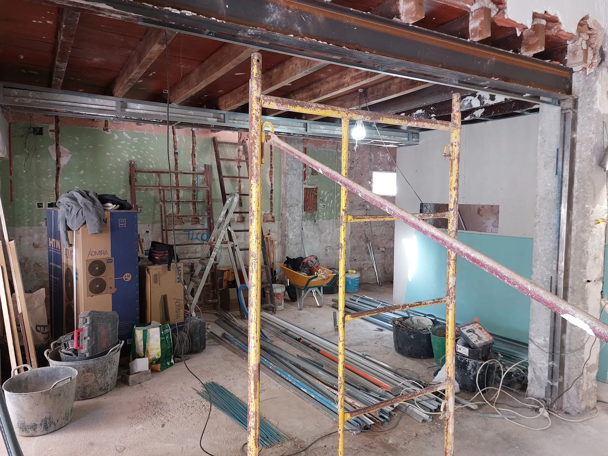 Zona de la barra del restaurante Los Dos en El Campello durante la obra: la nueva viga metálica recoge las antiguas vigas de madera del techo y descarga sobre un pilar reforzado, con un andamio en primer plano